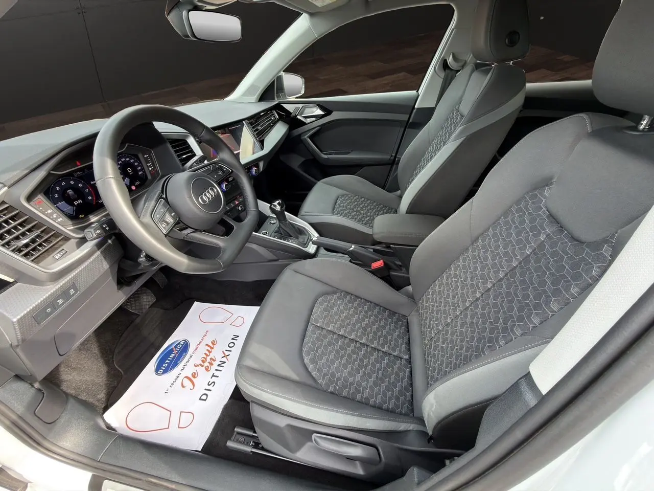 Vue intérieure côté conducteur de l’Audi A1 Sportback 2025 avec sièges tissu noir et tableau de bord moderne.