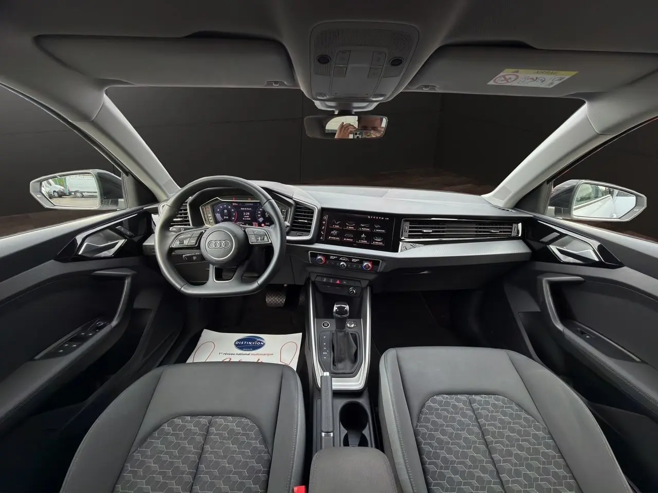 Vue intérieure avant de l'Audi A1 Sportback 2025 avec tableau de bord noir, volant sport cuir et écran tactile central.