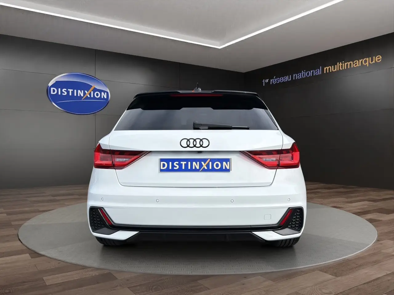 Vue arrière d'une Audi A1 Sportback blanche avec toit noir, feux LED et diffuseur arrière noir en showroom.