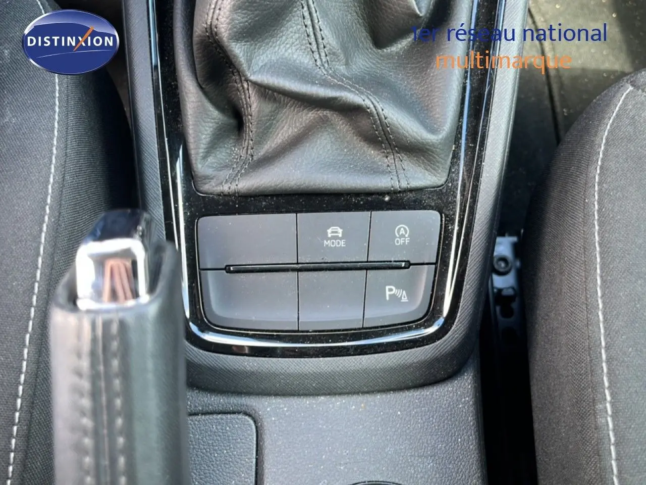 Gros plan sur la console centrale avec levier de frein à main et boutons de mode et assistance, intérieur tissu gris noir.