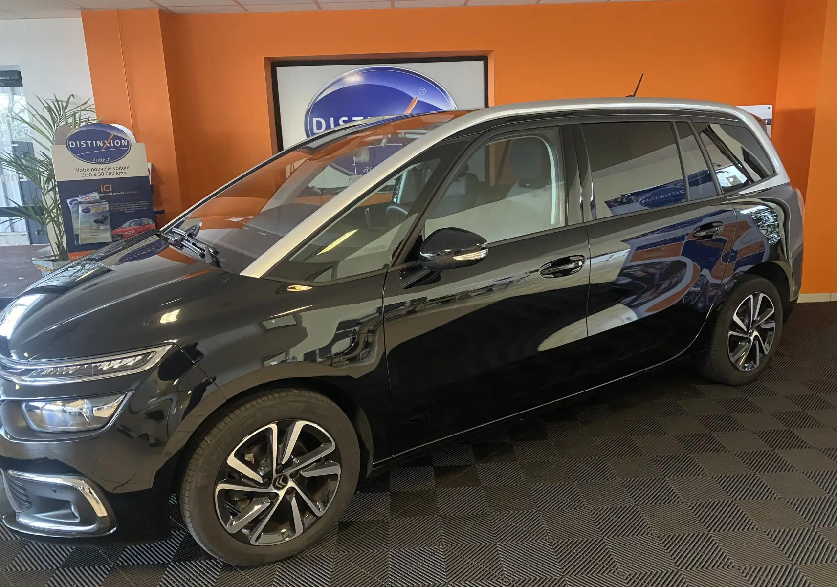 Vue de profil côté gauche d'un Citroën Grand C4 Spacetourer noir Perla avec jantes alliage 17" dans un showroom.