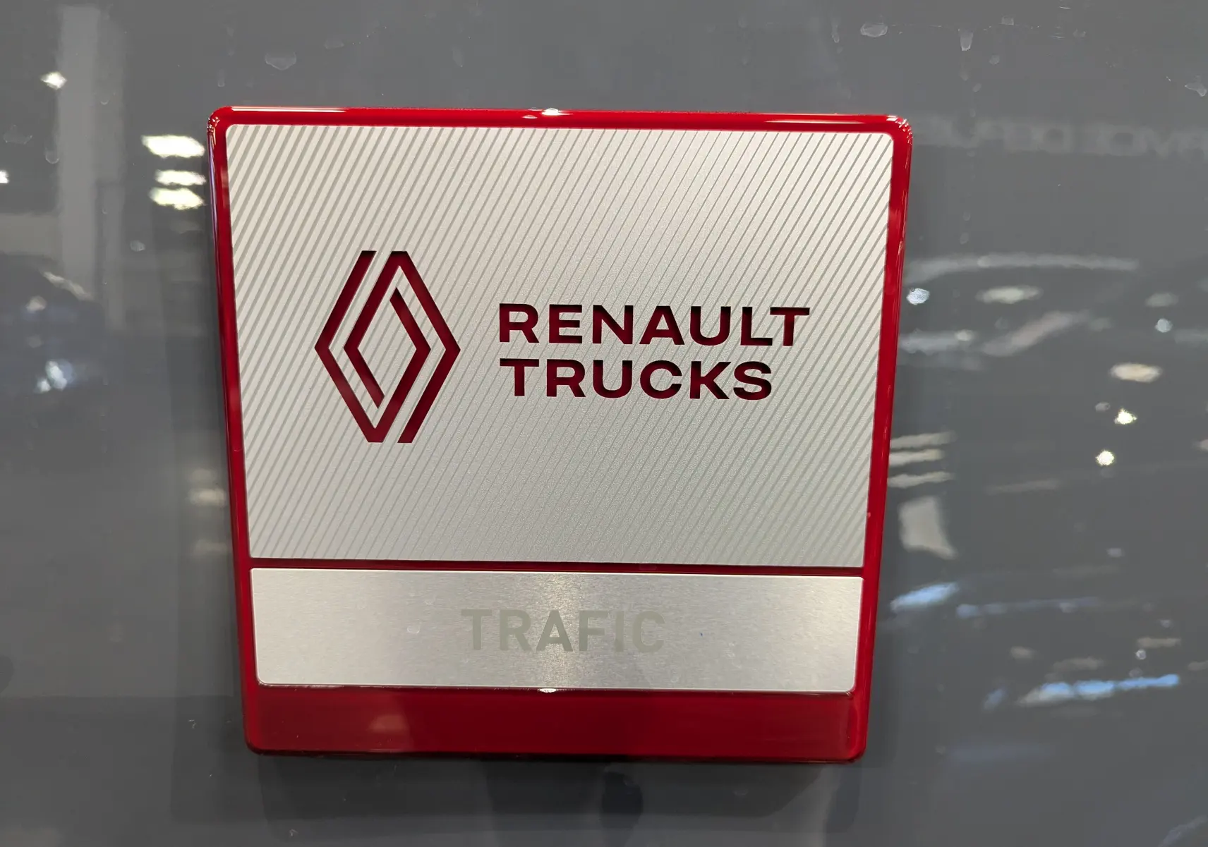 Gros plan sur le logo Renault Trucks rouge et argent fixé sur la carrosserie gris urbain du Trafic Fourgon.