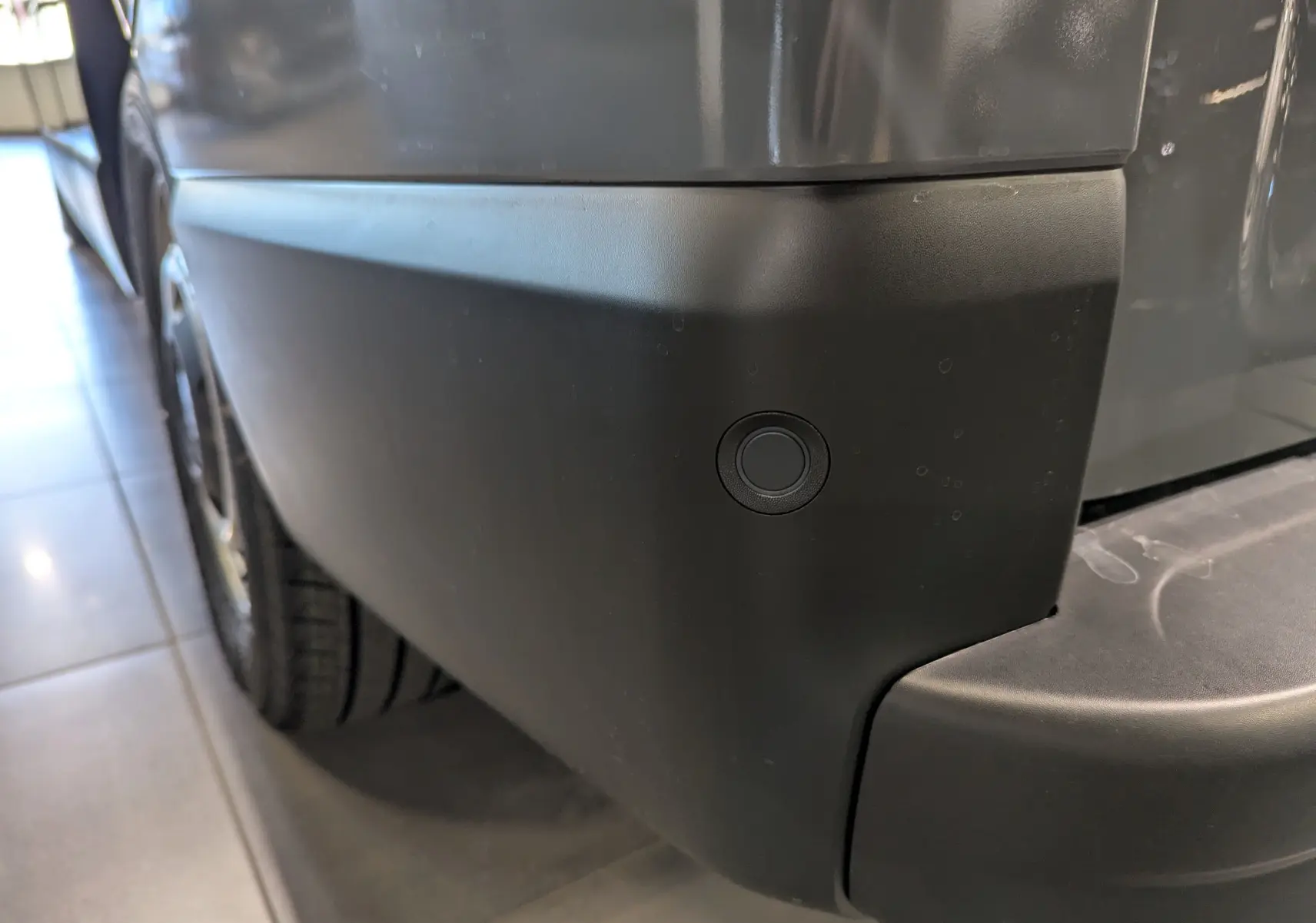 Gros plan sur le pare-chocs arrière droit gris urbain du Renault Trafic Fourgon avec capteur de recul intégré.