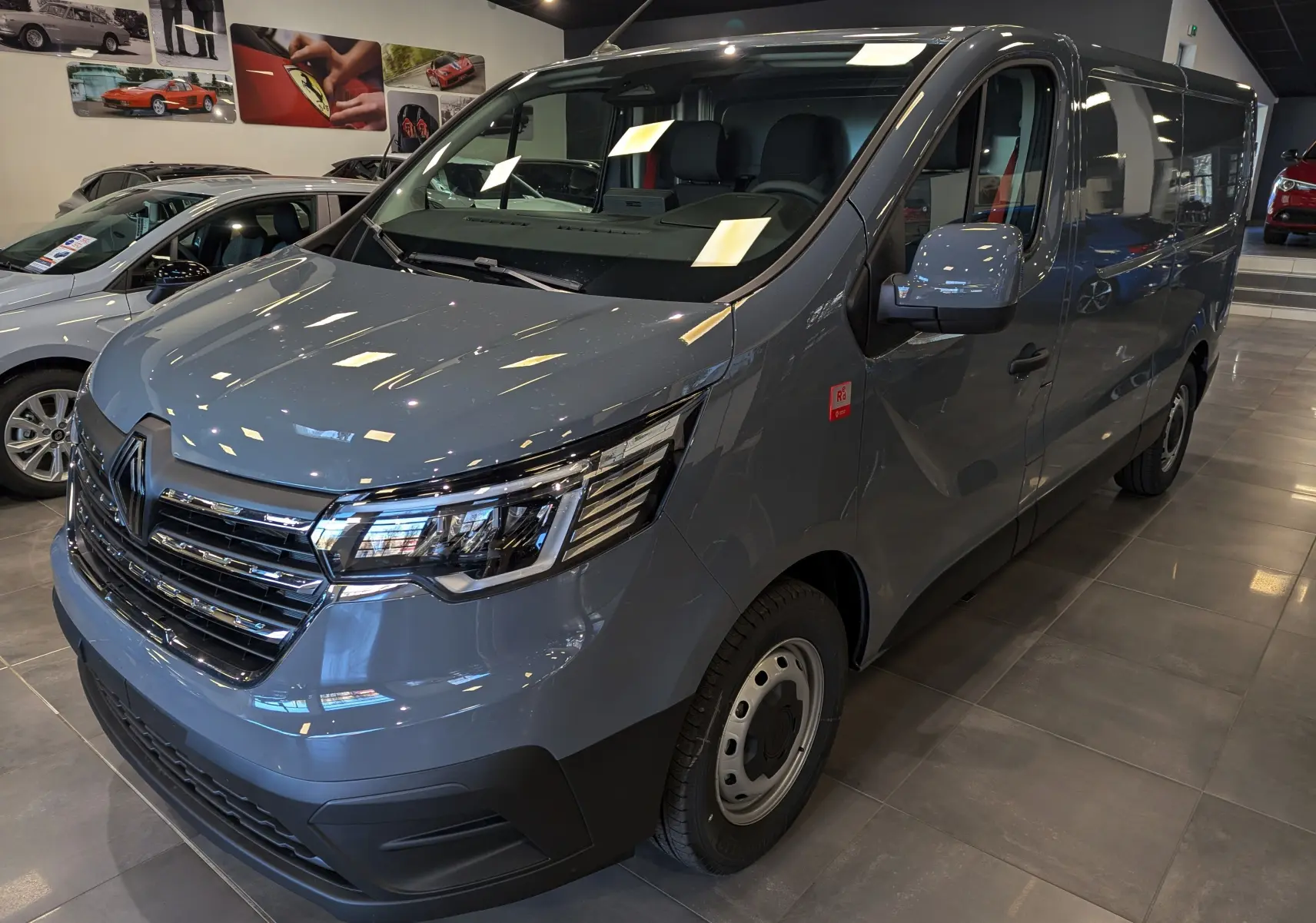 Renault Trafic Fourgon gris urbain en vue 3/4 avant droit dans un showroom, avec calandre chromée et phares LED.