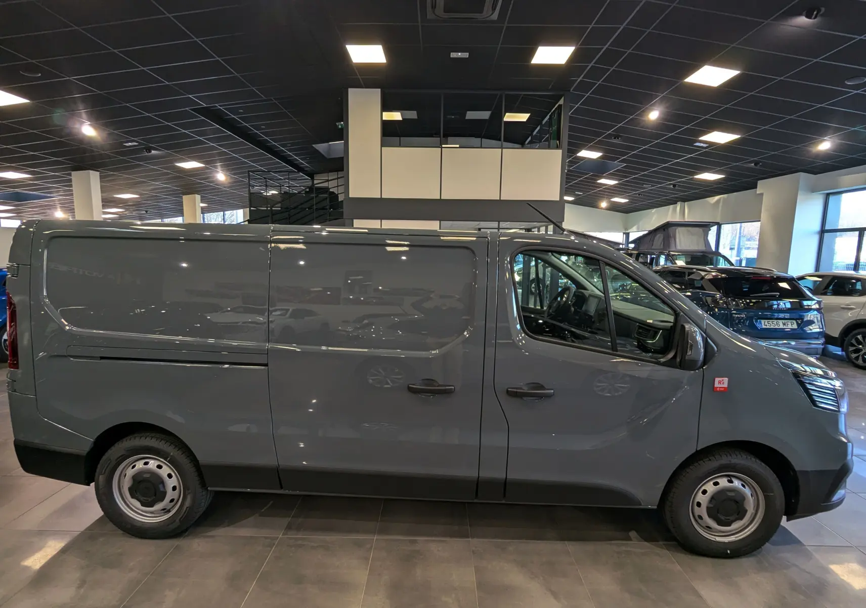 Renault Trafic Fourgon L2H1 2025 gris urbain vu de profil côté droit dans un showroom lumineux.