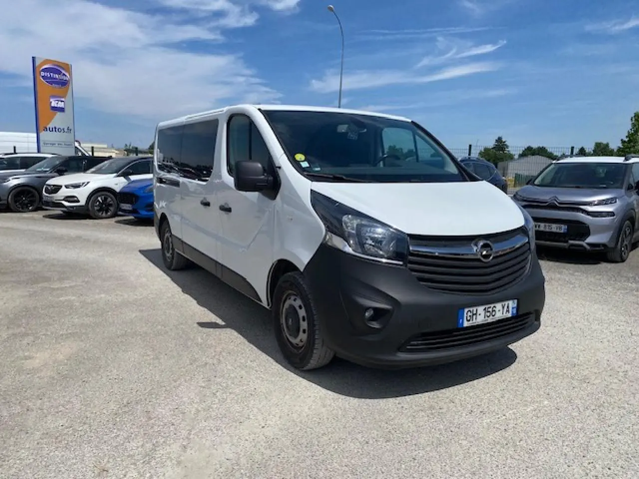 Opel Vivaro blanc vu en 3/4 avant droit, avec calandre noire et pare-chocs avant mat, stationné en extérieur.