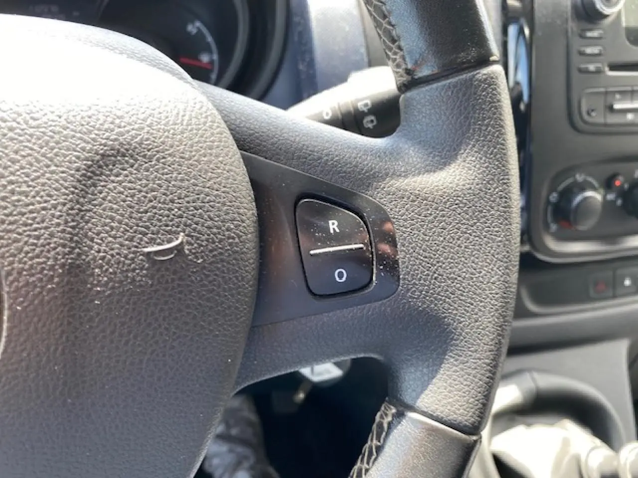 Gros plan sur le volant en cuir noir de l'Opel Vivaro blanc, avec commandes intégrées visibles à droite.