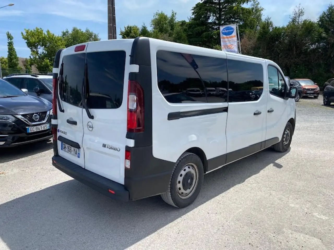 Vue 3/4 arrière droite d'un Opel Vivaro blanc, combi rallongé avec vitres teintées et portes arrière battantes.