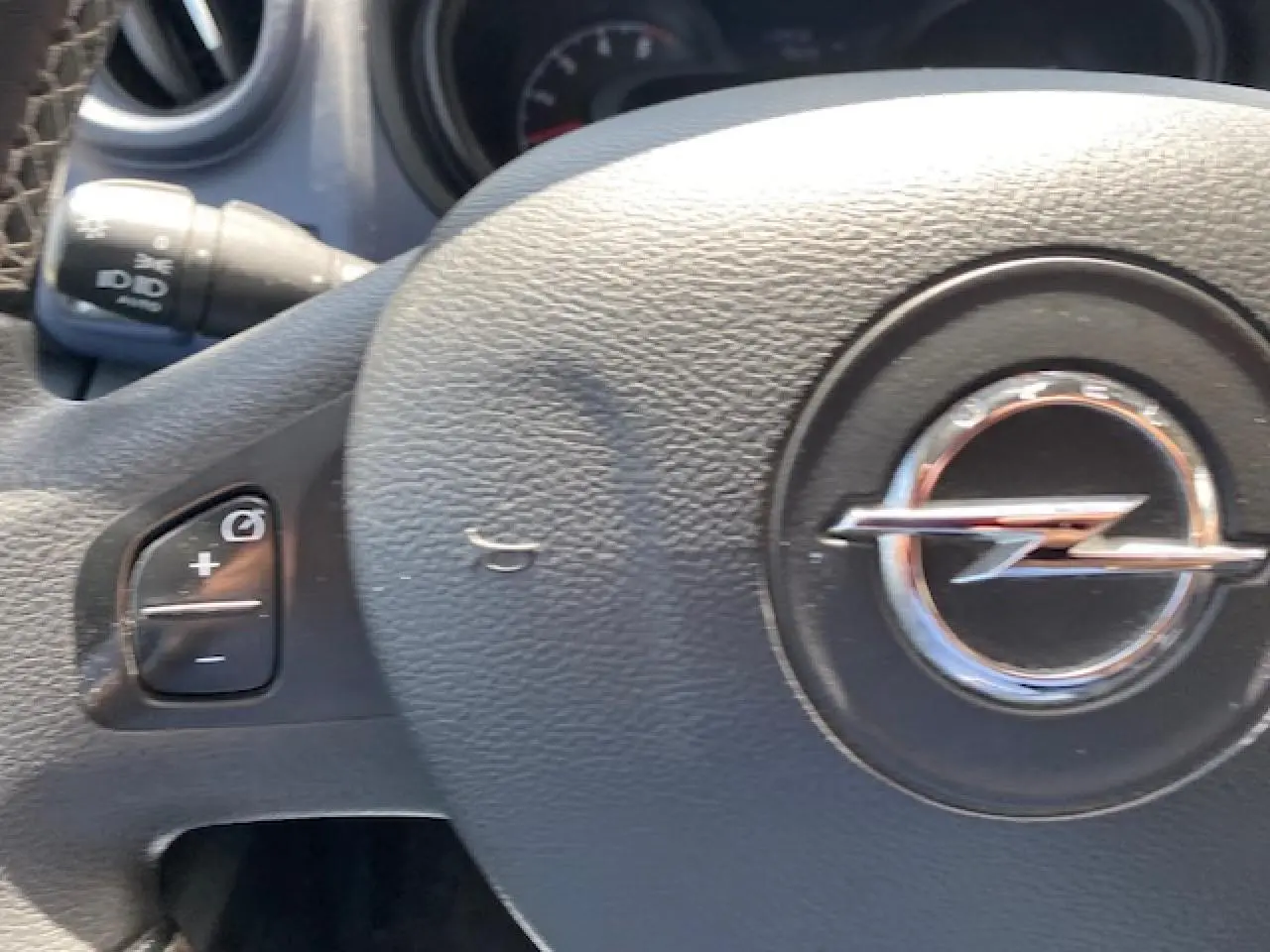 Gros plan sur le volant noir avec logo Opel en relief et commandes de régulateur de vitesse visibles sur la gauche.