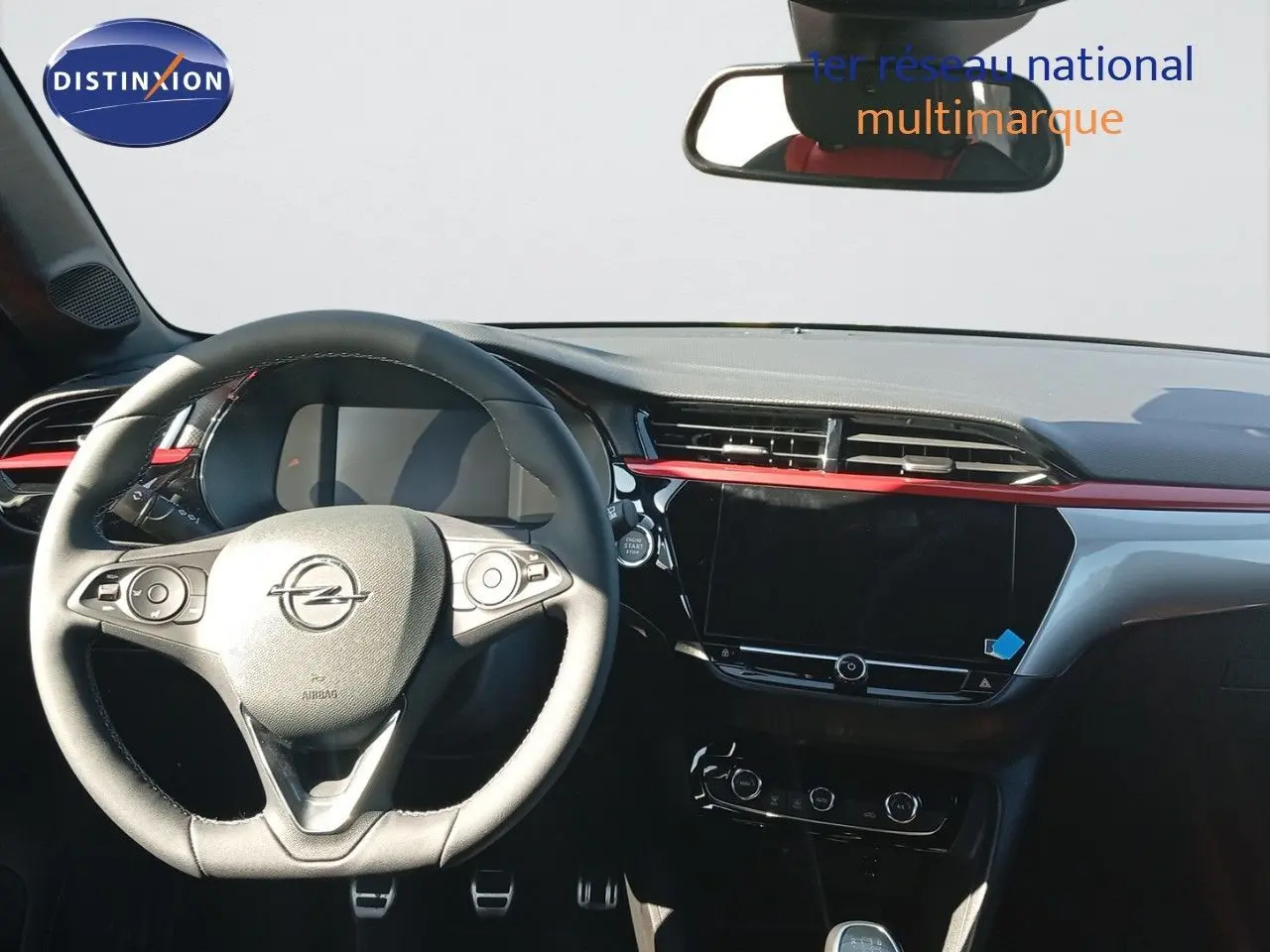 Intérieur de l’Opel Corsa 2023 avec volant cuir, tableau de bord noir et bande décorative rouge côté conducteur.