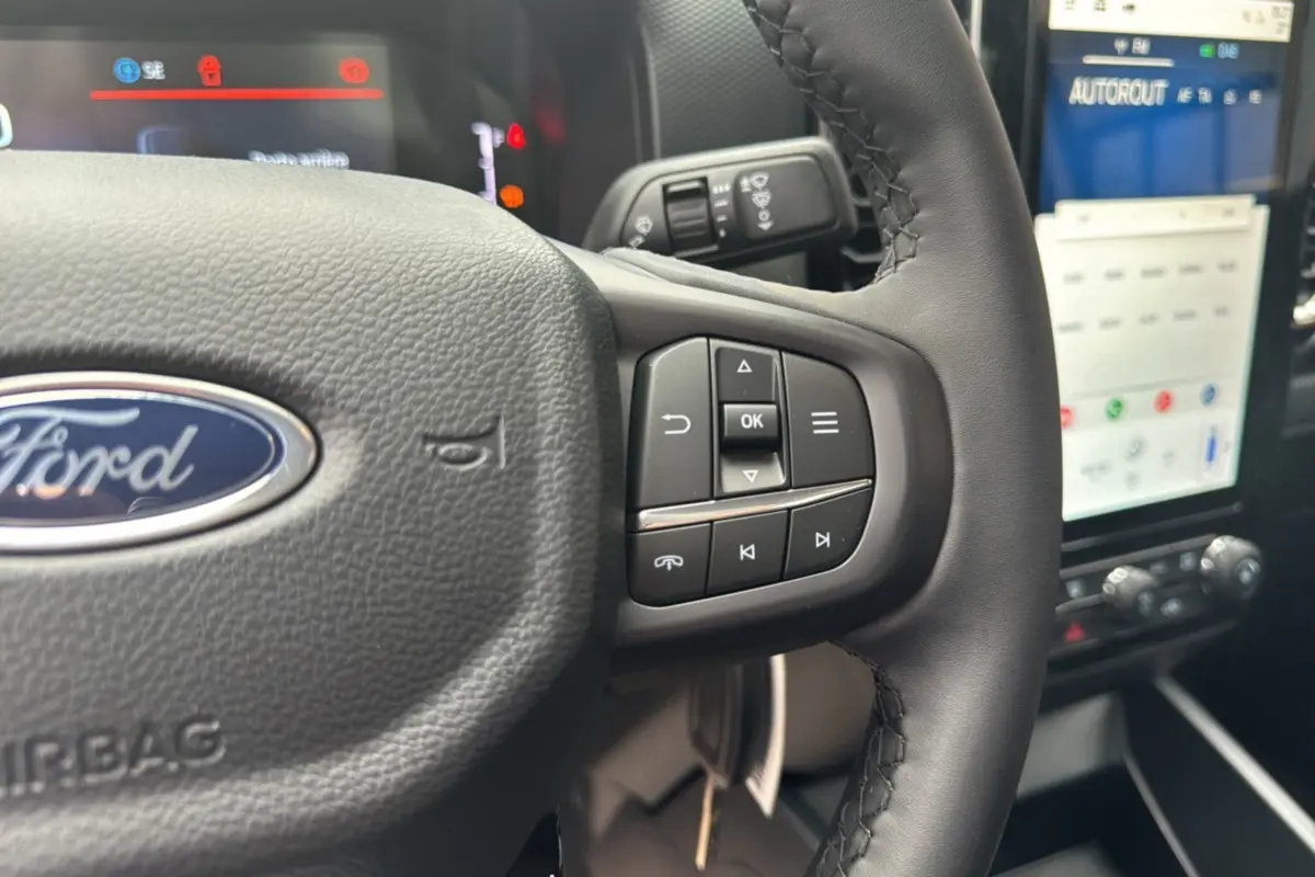 Gros plan sur le volant cuir multifonctions du Ford Ranger blanc glacier, avec commandes intégrées et écran tactile en arrière-plan.