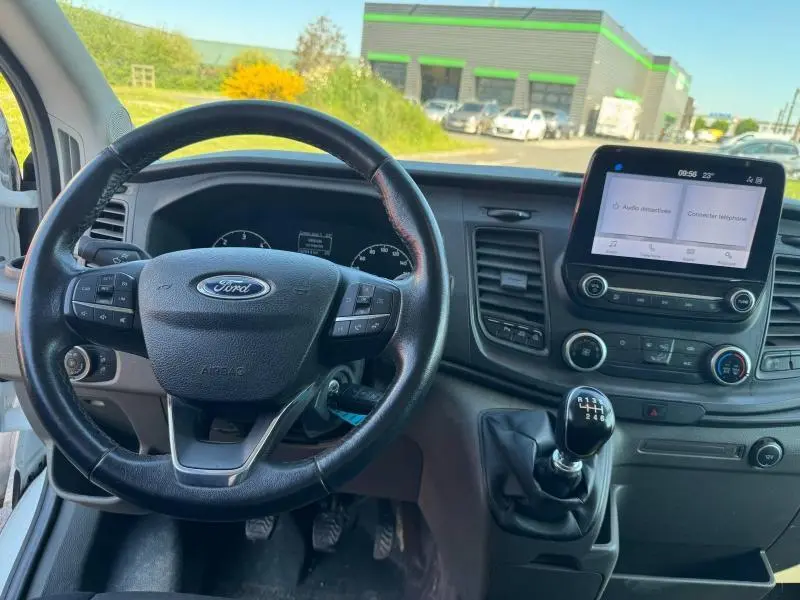 Vue intérieure du tableau de bord du Ford Transit Fourgon blanc glacier 2020, volant multifonction et écran tactile central.