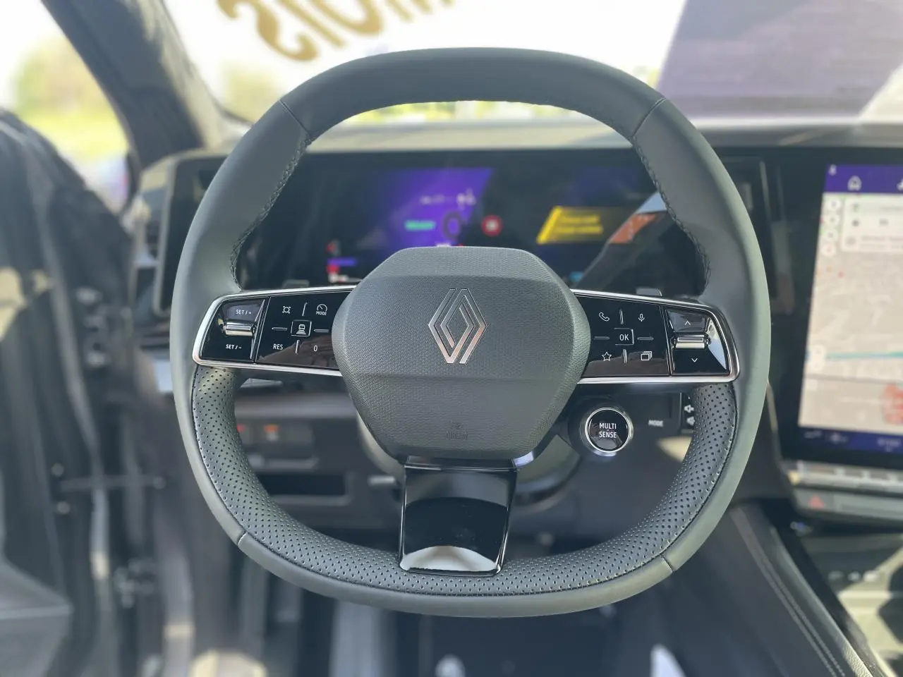 Volant Renault RAFALE 2025 en textile refined avec commandes intégrées, cadrans numériques et écran tactile visible en arrière-plan.