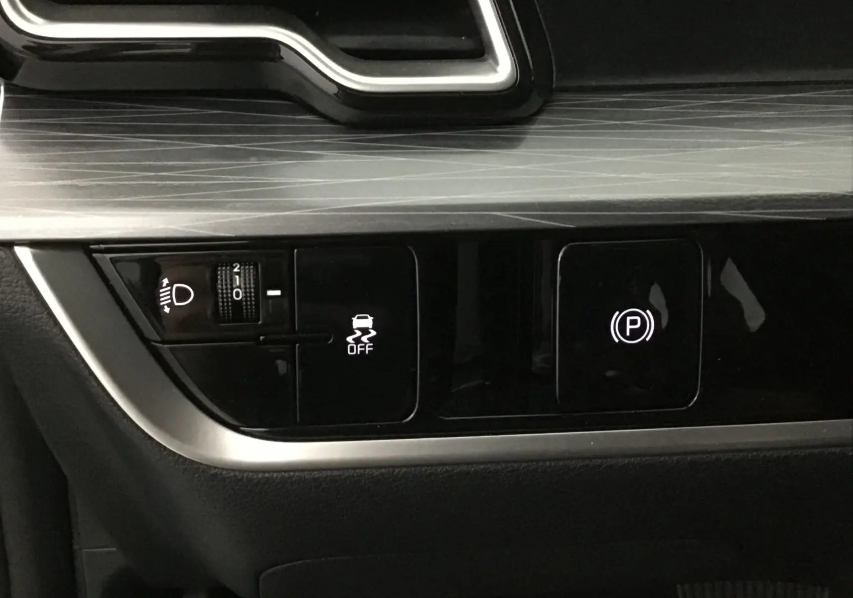 Détail du tableau de bord du Kia Sportage gris Sirius 2025 montrant les commandes d'éclairage et frein à main électronique.