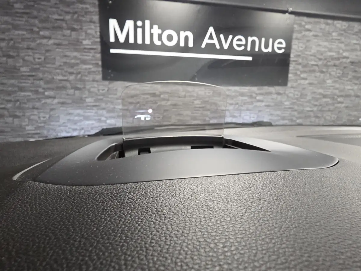 Affichage tête haute transparent sur le tableau de bord noir du Renault Scenic blanc, avec fond mural gris et panneau Milton Avenue.