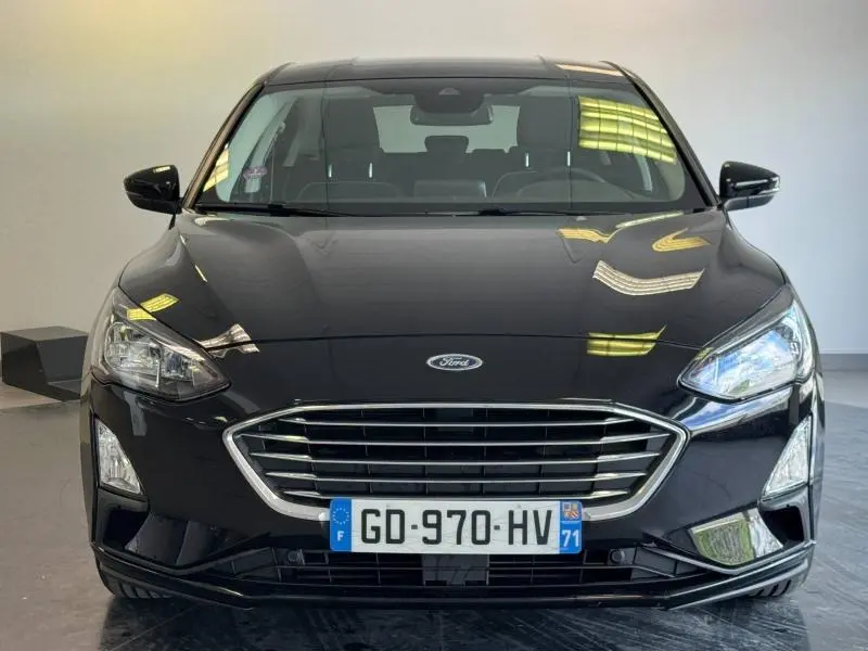 Vue frontale d'une Ford Focus noire Agate métallisé avec calandre chromée et phares LED allumés.