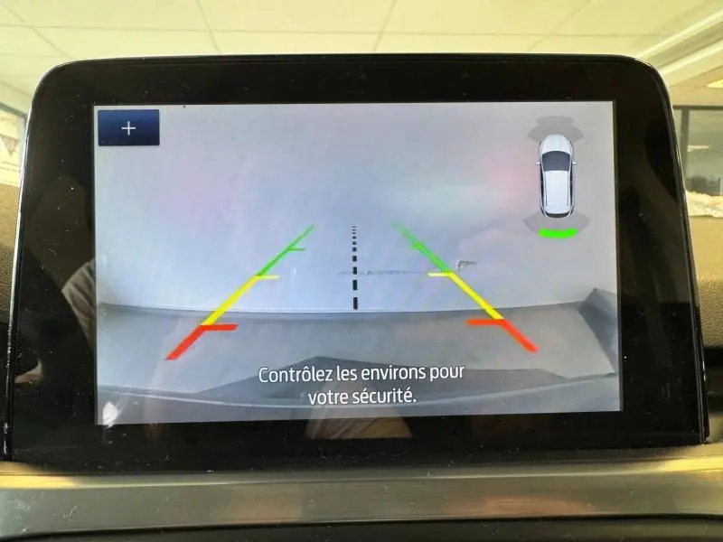 Affichage de la caméra de recul sur l'écran tactile d'une Ford Focus noire, avec repères colorés et vue arrière du véhicule.
