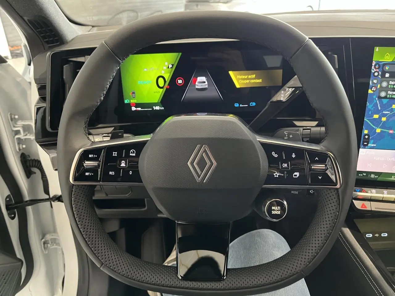 Vue intérieure centrée sur le volant noir perforé de la Renault Rafale blanche avec tableau de bord numérique et écran tactile.