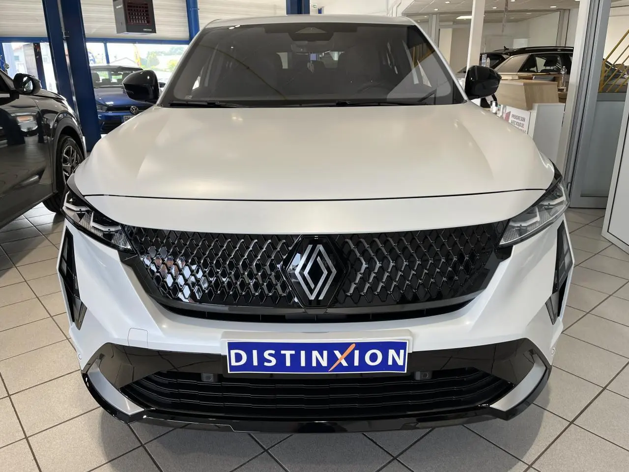 Vue frontale du Renault Rafale blanc avec calandre noire à motif 3D et logo central brillant dans un showroom.