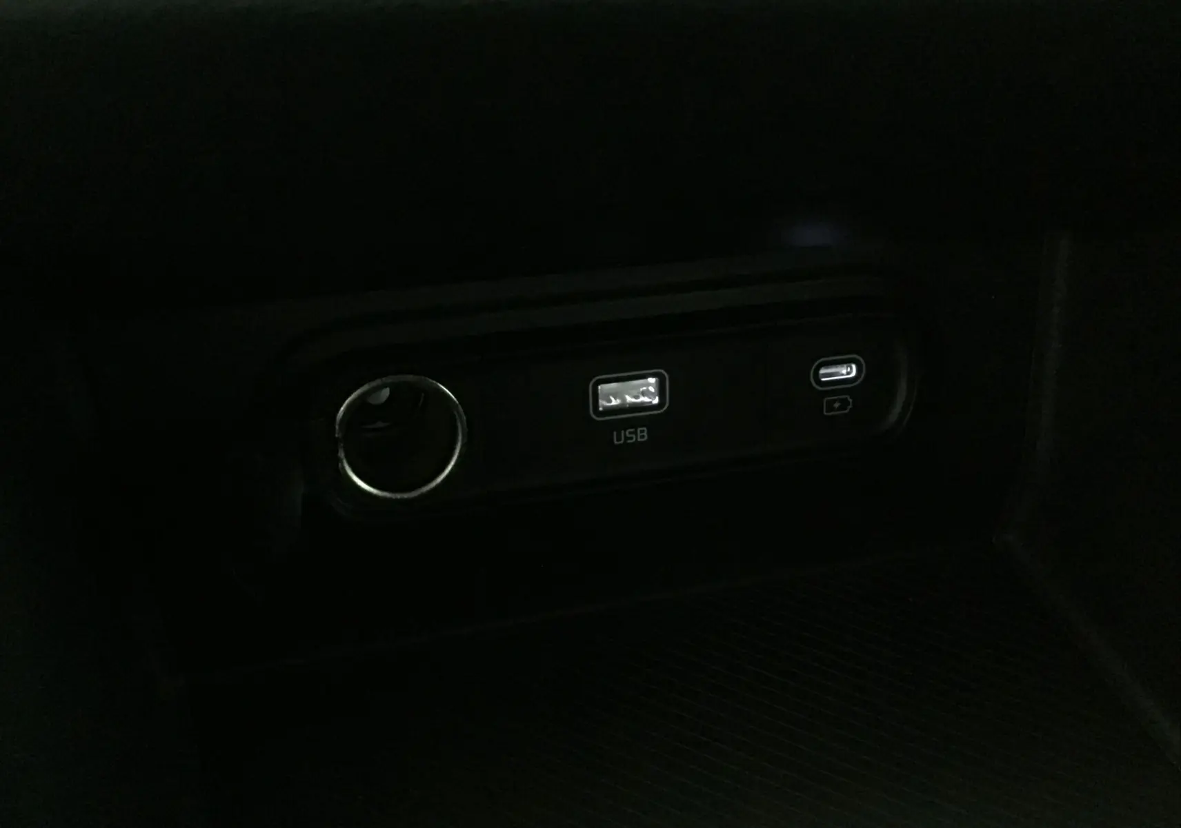 Prise USB et port allume-cigare dans l'habitacle sombre du Kia Sportage gris Sirius 2025.