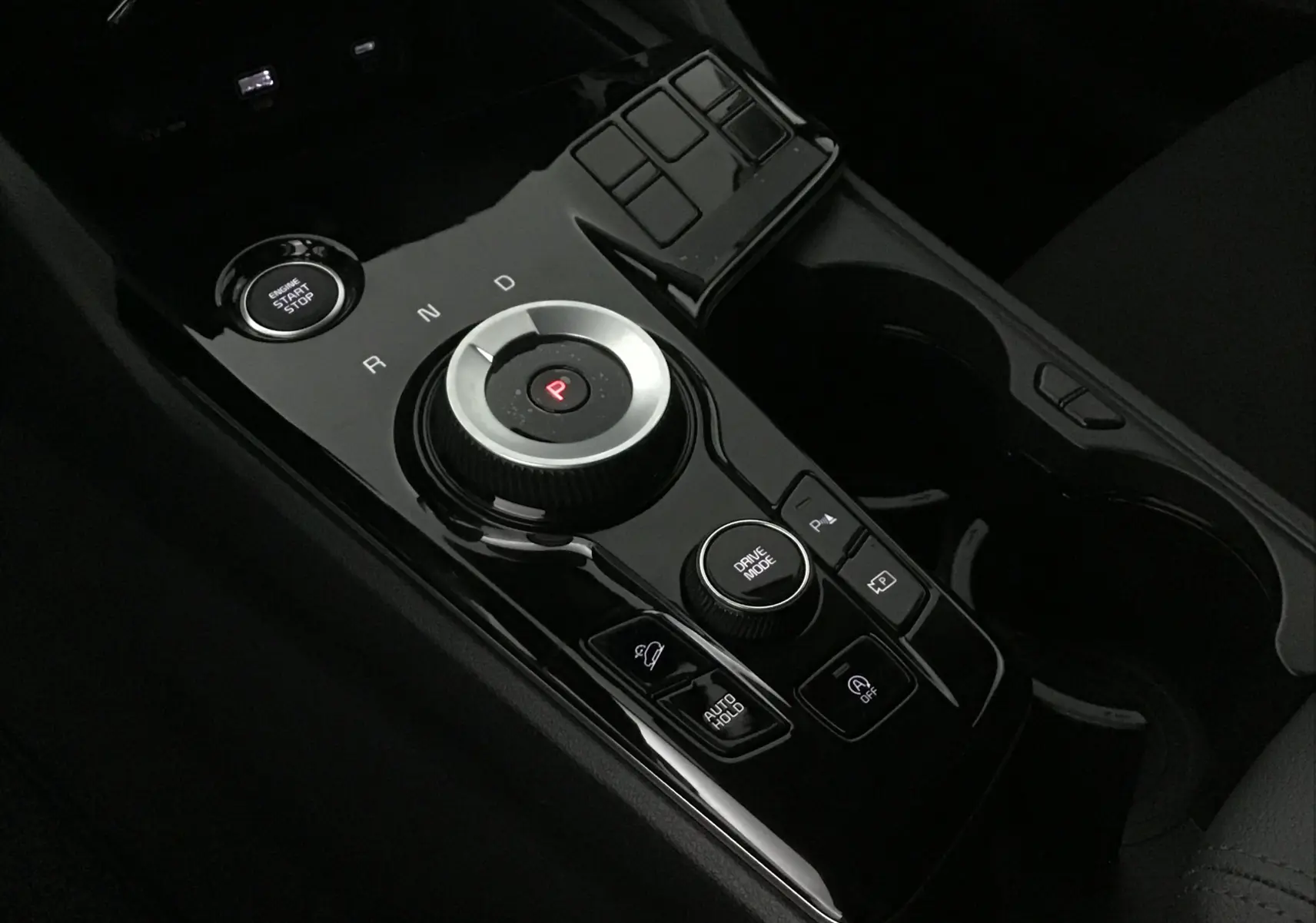 Gros plan sur la console centrale noire brillante du Kia Sportage 2025 avec molette de boîte auto et bouton start/stop.