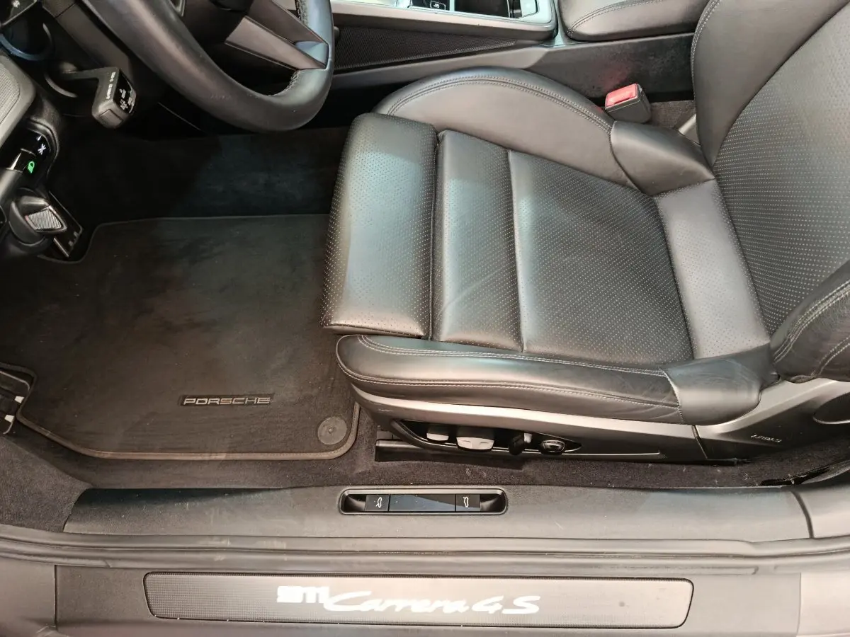 Vue intérieure côté conducteur de la Porsche 911 Carrera 4S 2019, siège cuir noir et tapis avec logo Porsche.