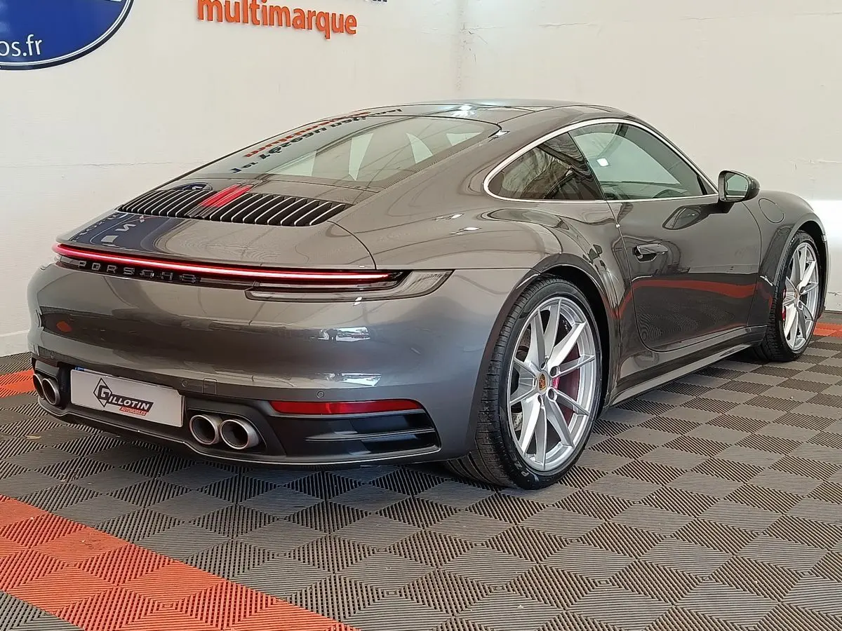 Vue 3/4 arrière droite d'une Porsche 911 Carrera 4S Coupé gris foncé avec quadruple sortie d'échappement et feux LED continus.
