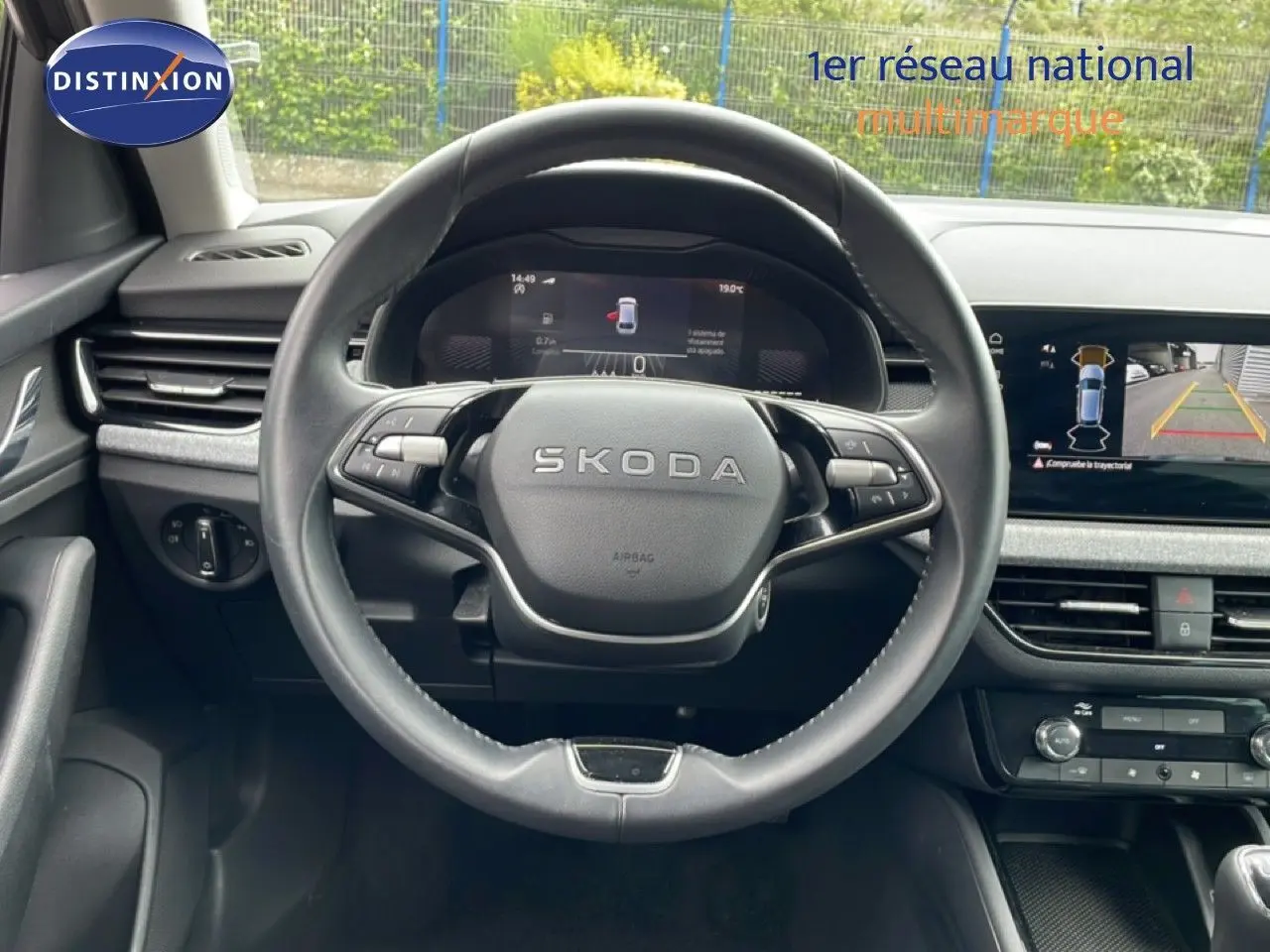 Vue intérieure centrée sur le volant SKODA noir avec tableau de bord numérique et écran de caméra de recul.