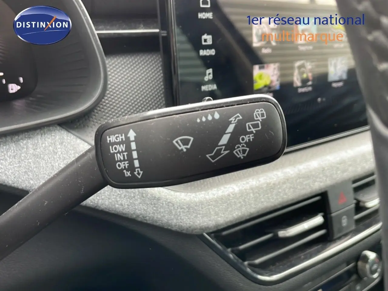 Gros plan sur la commande d’essuie-glace dans l’habitacle d’une Skoda Scala noir magique métal, avec écran tactile en arrière-plan.