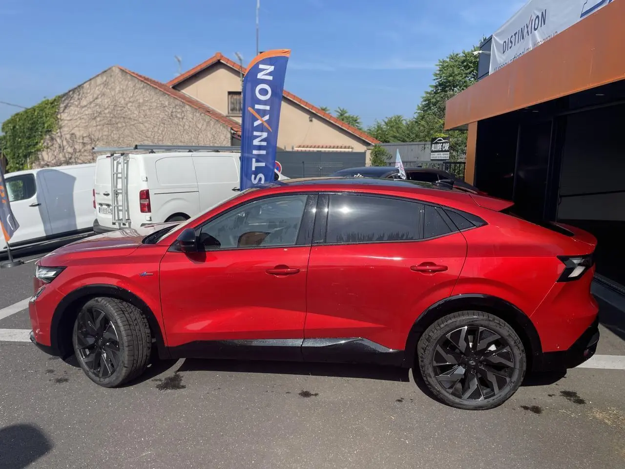 Profil côté gauche de la Renault Rafale rouge à toit noir, avec jantes noires et vitres teintées, stationnée en extérieur.