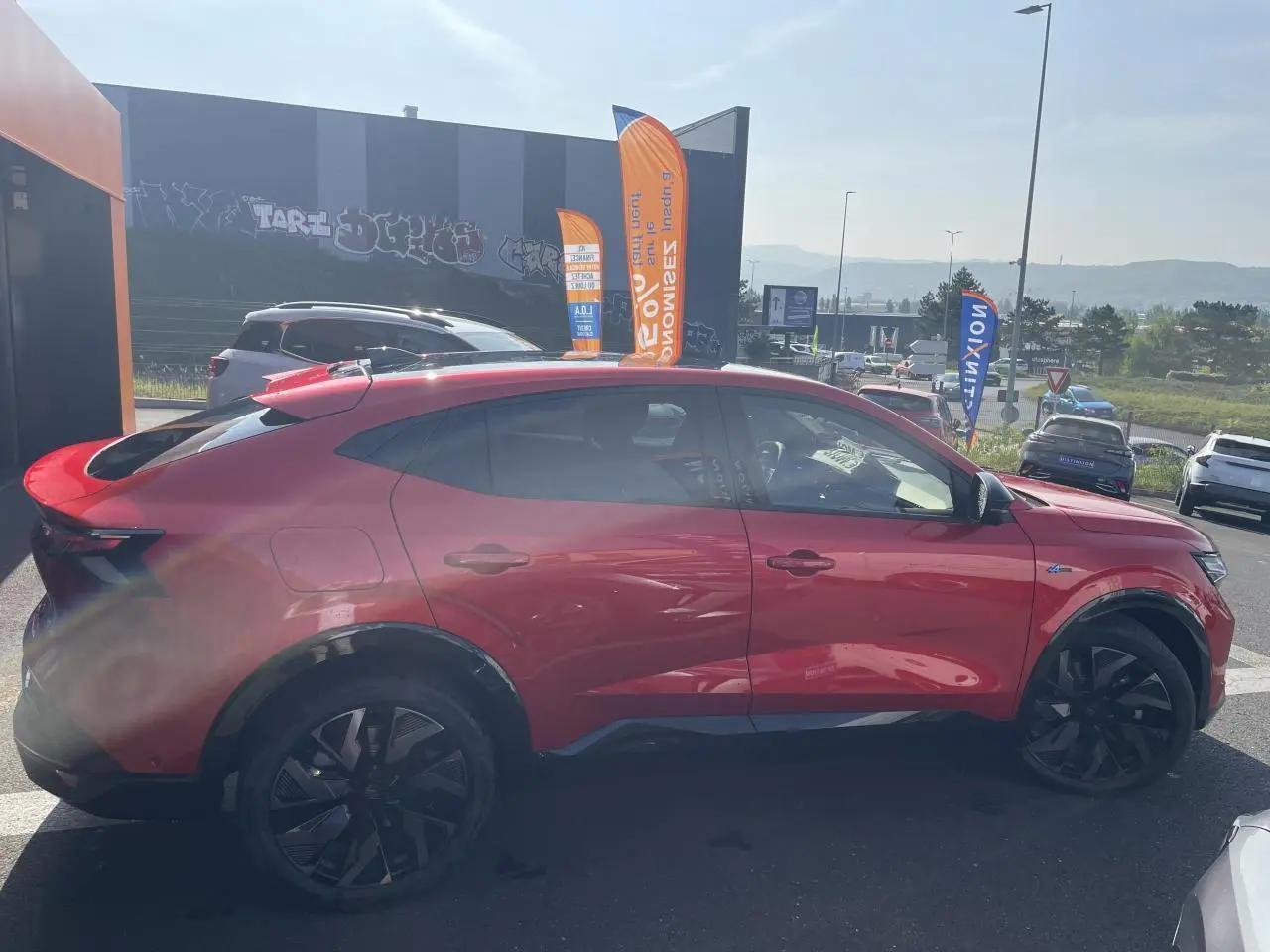 Profil côté gauche d'un Renault Rafale rouge à toit noir avec jantes noires et badge Esprit Alpine visible.