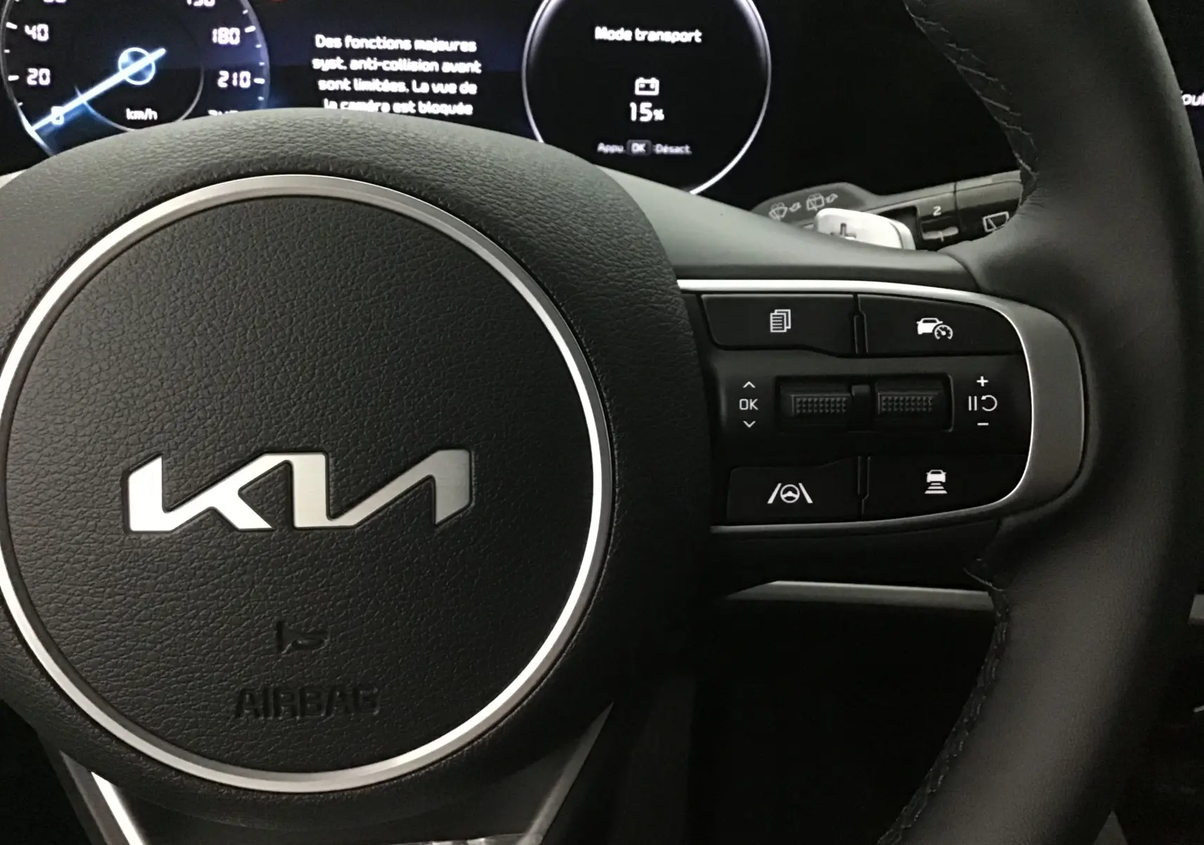 Gros plan sur le volant cuir du Kia Sportage 2025 avec commandes multifonctions côté droit et écran digital en arrière-plan.