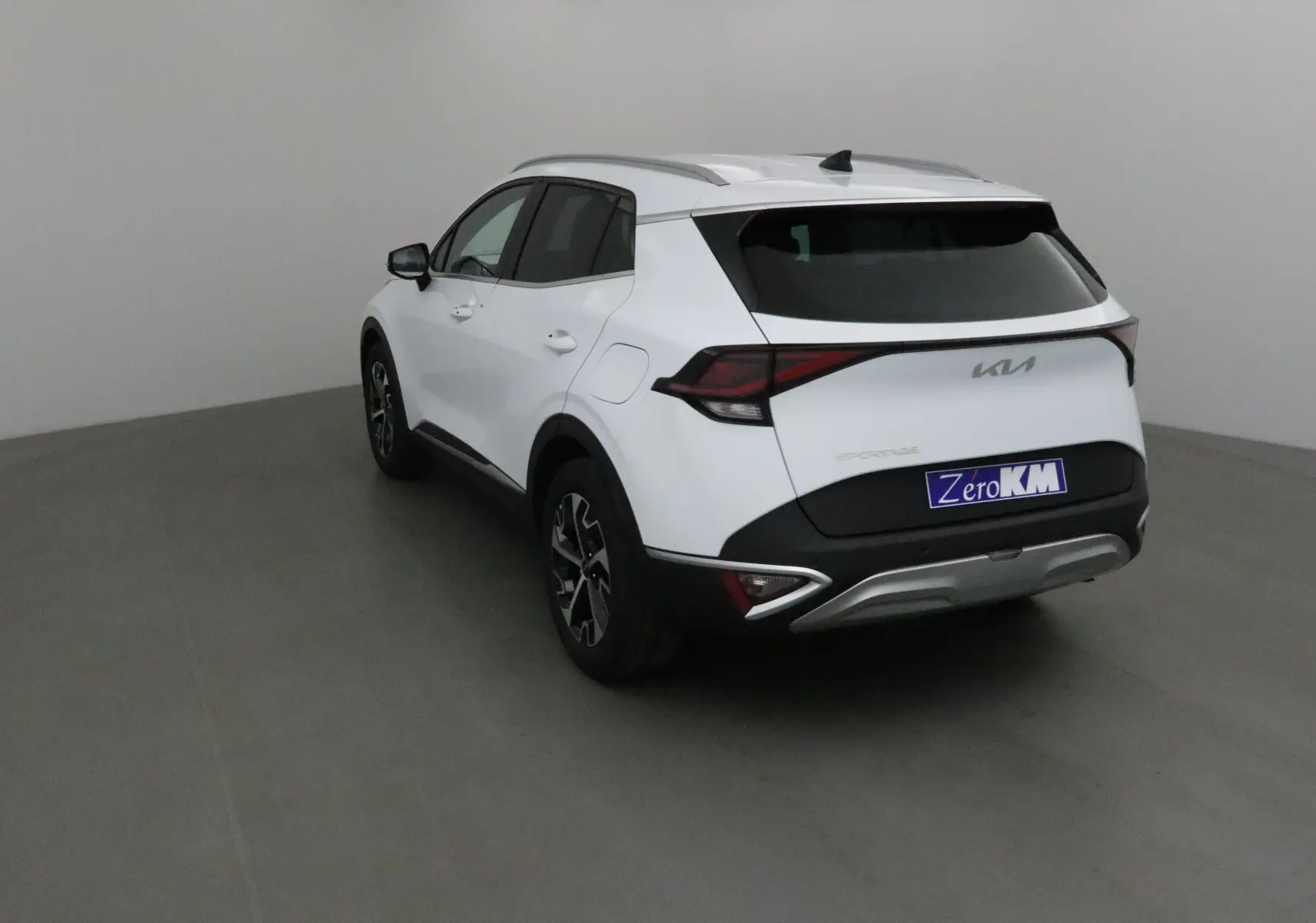 KIA Sportage blanc vu en 3/4 arrière gauche, avec feux arrière LED et jantes alliage noires.