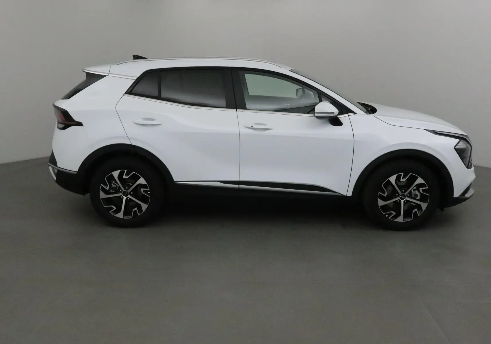 Profil côté droit du KIA SPORTAGE blanc 2025 avec jantes noires et détails noirs contrastants.