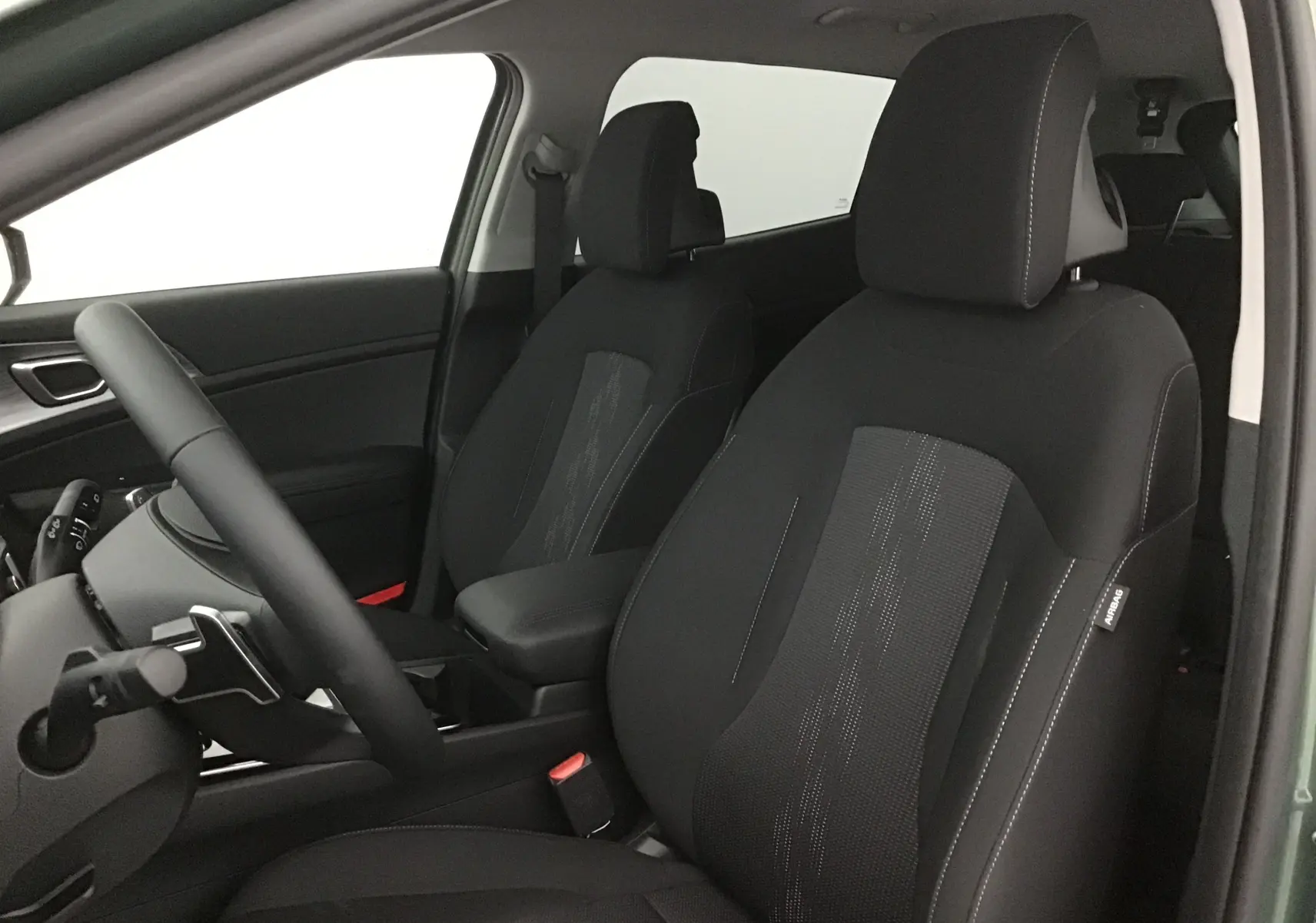 Vue intérieure côté conducteur du Kia Sportage blanc 2025, sièges noirs avec surpiqûres et accoudoir central.