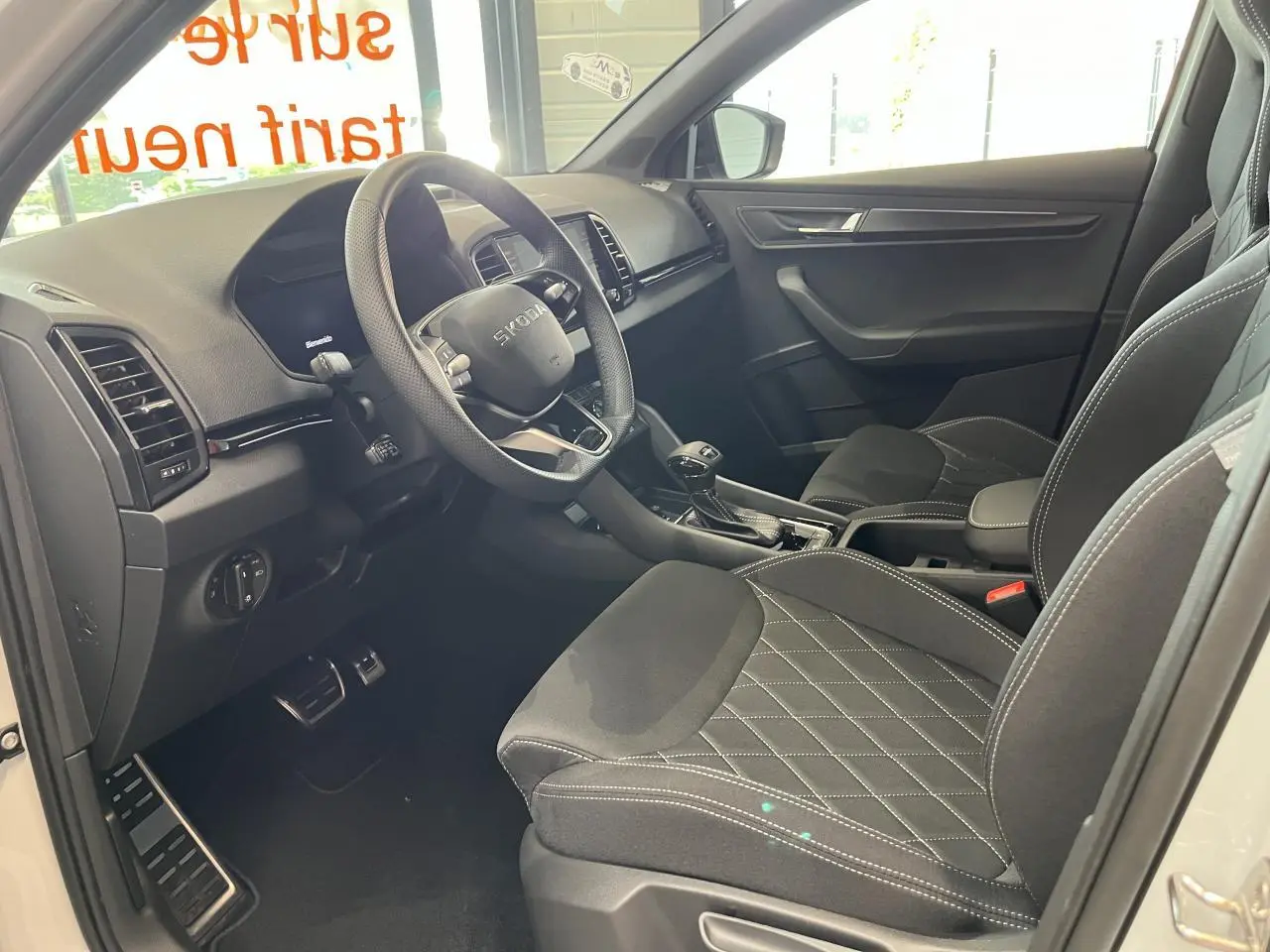 Intérieur avant droit du Skoda Karoq blanc 2025, sellerie noire Sportline avec surpiqûres blanches et volant cuir multifonctions.