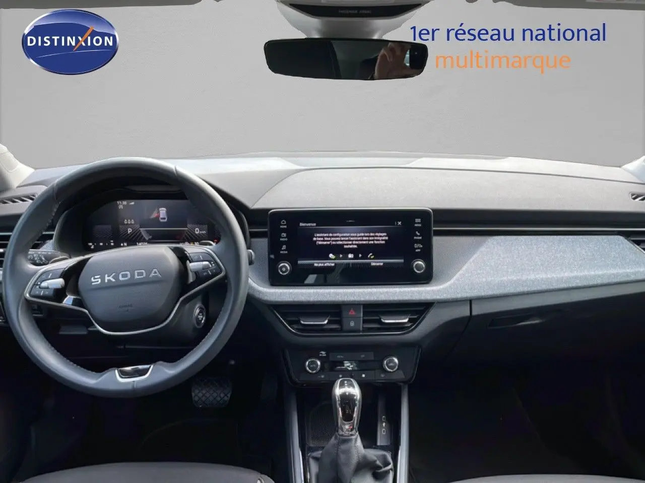Vue intérieure frontale du tableau de bord gris clair et noir du Skoda Scala blanc glacier avec écran tactile et volant multifonction.
