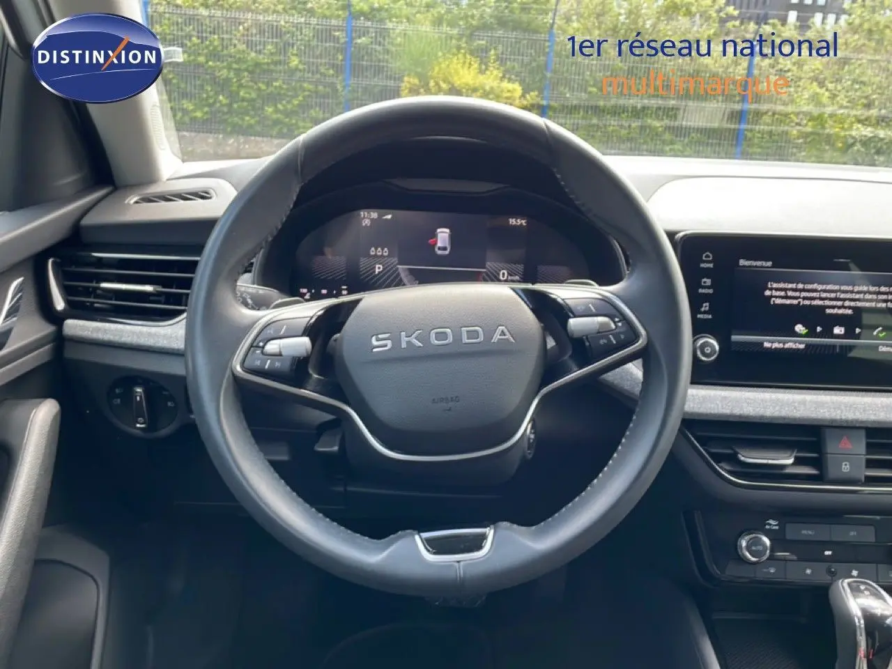 Vue intérieure centrée sur le volant noir SKODA avec tableau de bord digital et écran tactile sur fond gris.