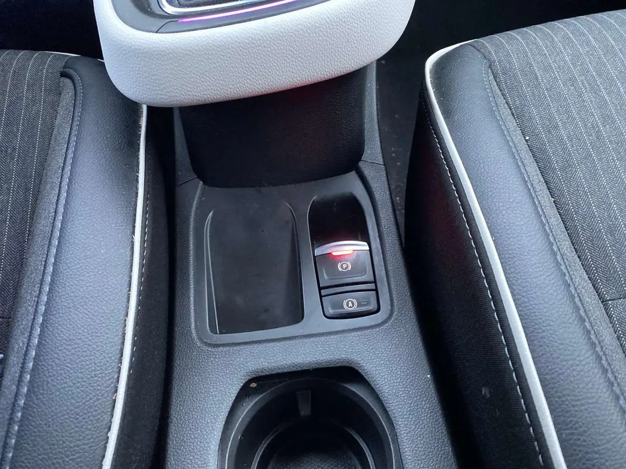 Gros plan sur la console centrale de la Renault Clio blanche 2023, montrant le frein à main électrique et les sièges noirs à surpiqûres blanches.