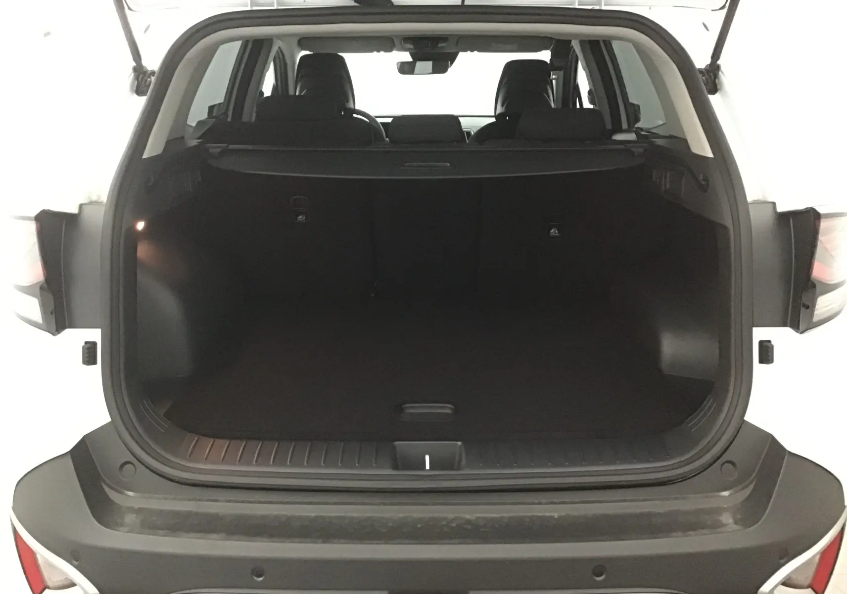 Coffre ouvert d'un Kia Sportage blanc 2025, vue arrière, montrant l'espace de chargement vide et les sièges noirs.