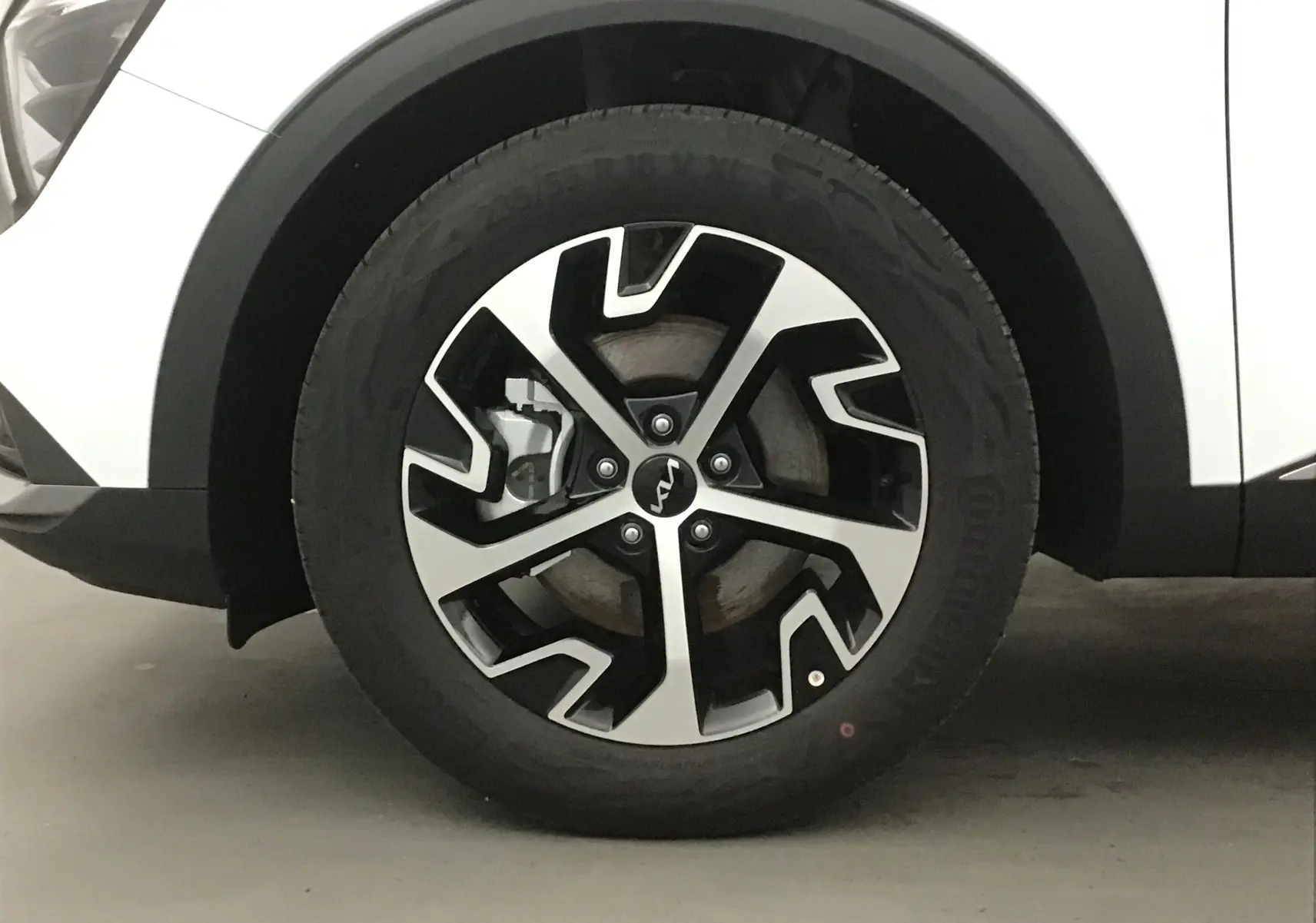 Gros plan sur la roue avant gauche du Kia Sportage blanc 2025, mettant en valeur la jante alliage bicolore au design moderne.