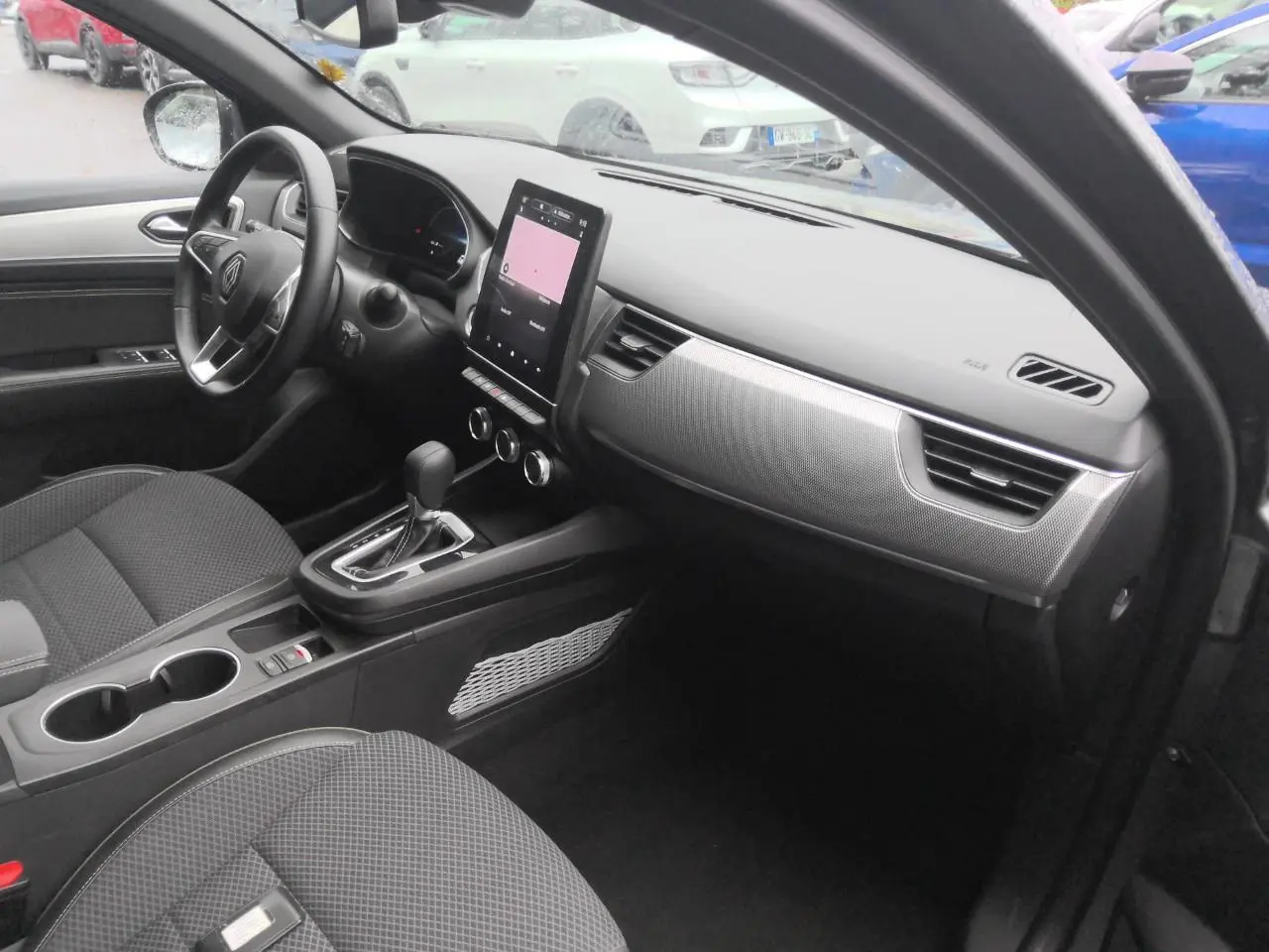 Intérieur avant droit du Renault Arkana 2024 gris métal, tableau de bord moderne avec écran tactile vertical.