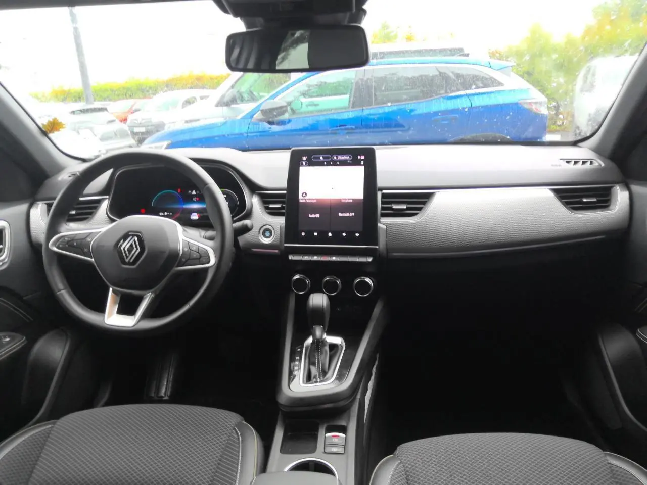 Intérieur du Renault Arkana 2024, vue avant du tableau de bord avec écran tactile vertical et volant en textile noir.