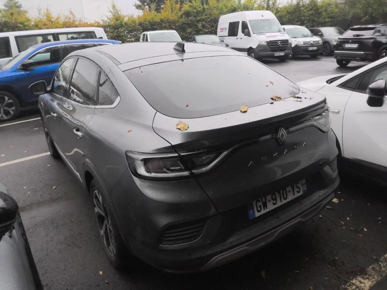 Vue 3/4 arrière d'un Renault Arkana gris métal foncé avec toit ouvrant, garé en extérieur sous un ciel couvert.