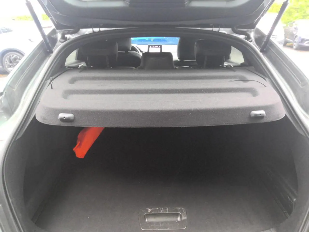 Coffre ouvert vu de l'arrière du Renault Arkana gris métal foncé, avec cache-bagages et intérieur sombre.