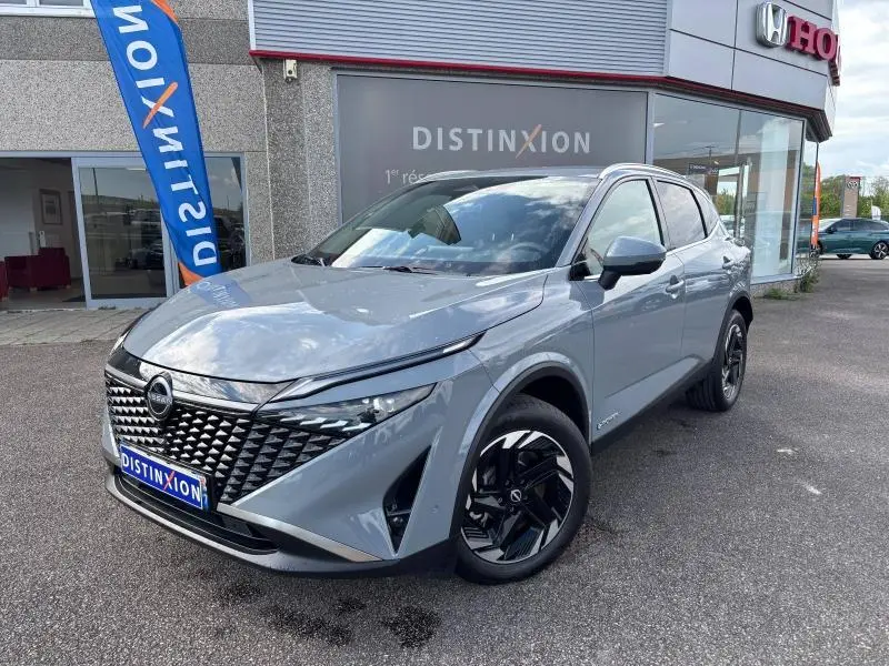 Nissan Qashqai e-POWER gris Argile en 3/4 avant droit, avec calandre distinctive et jantes noires brillantes.
