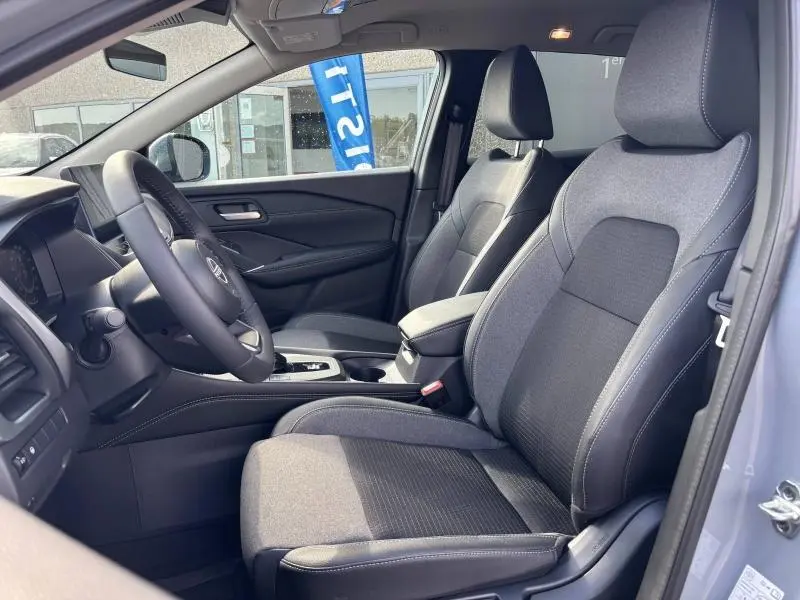 Vue intérieure côté conducteur du Nissan Qashqai e-POWER 2024 gris Argile, sièges tissu noir avec accoudoir central.