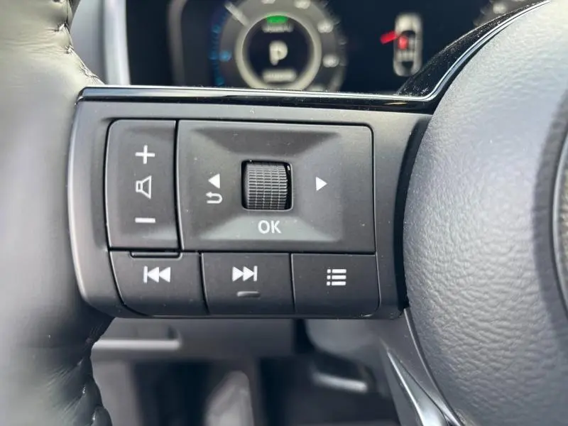 Gros plan sur les commandes multifonctions au volant cuir noir du Nissan Qashqai e-POWER 2024, avec écran digital en arrière-plan.