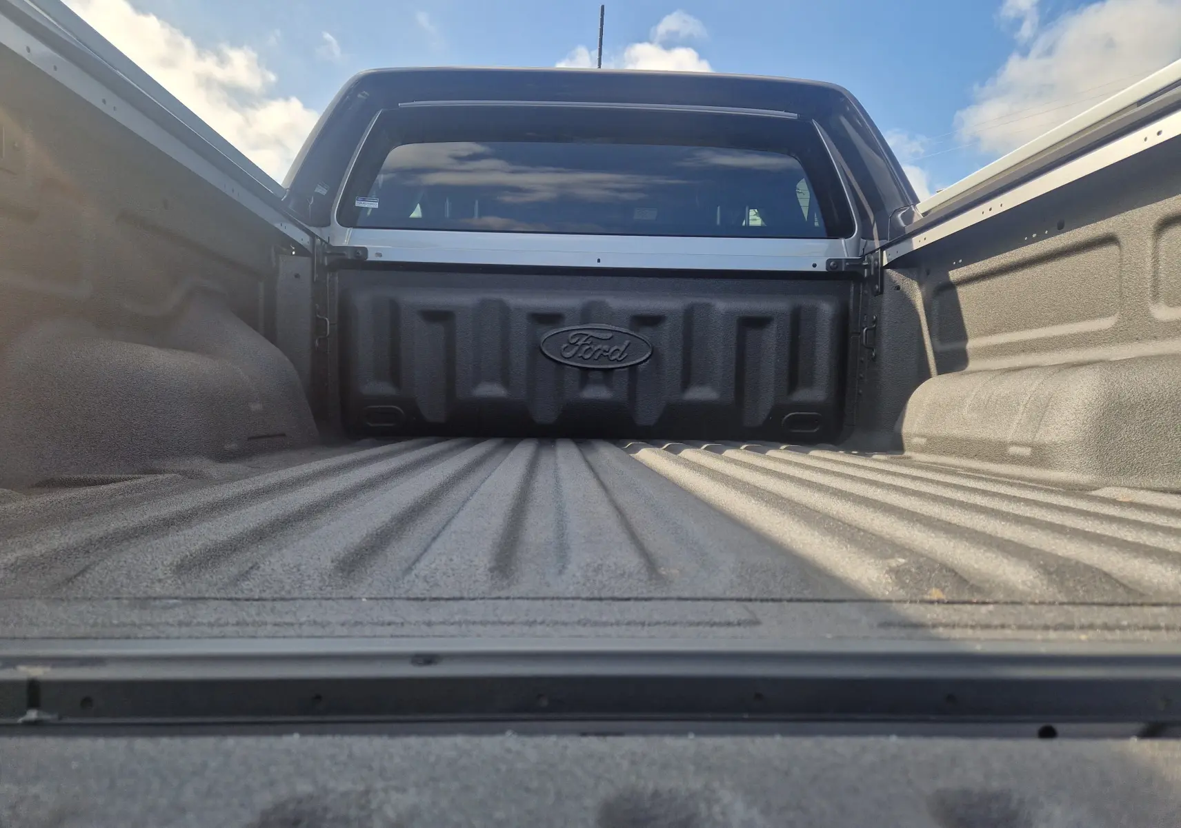 Vue rapprochée de la benne gris Iconic du Ford Ranger Super Cabine 2025 avec protection plastique et logo Ford visible.