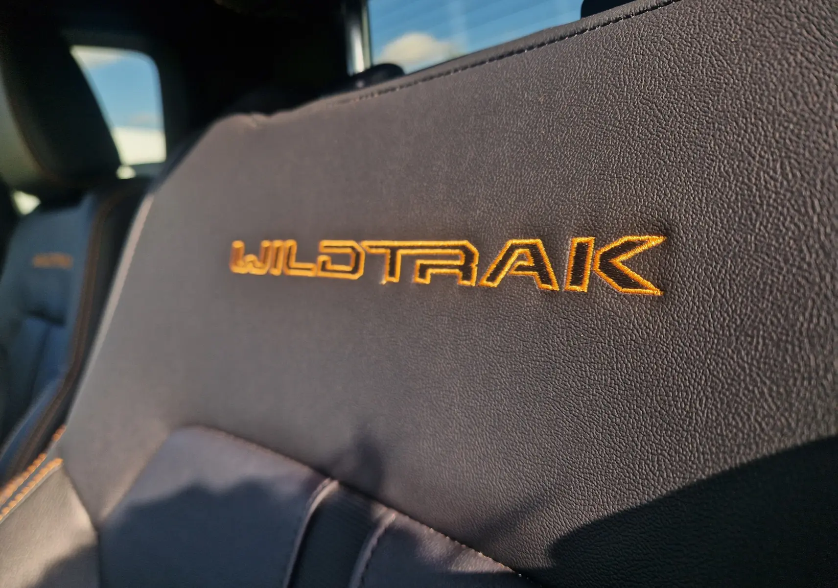 Gros plan sur l'appui-tête en cuir noir avec broderie orange Wildtrak à l'intérieur du Ford Ranger Super Cabine gris Iconic.